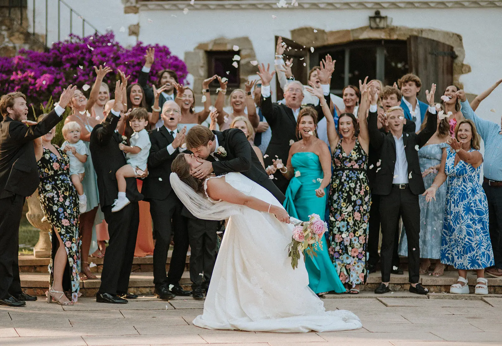 Invitados aplaudiendo mientras los novios se besan en una terraza soleada en una finca de Cataluña