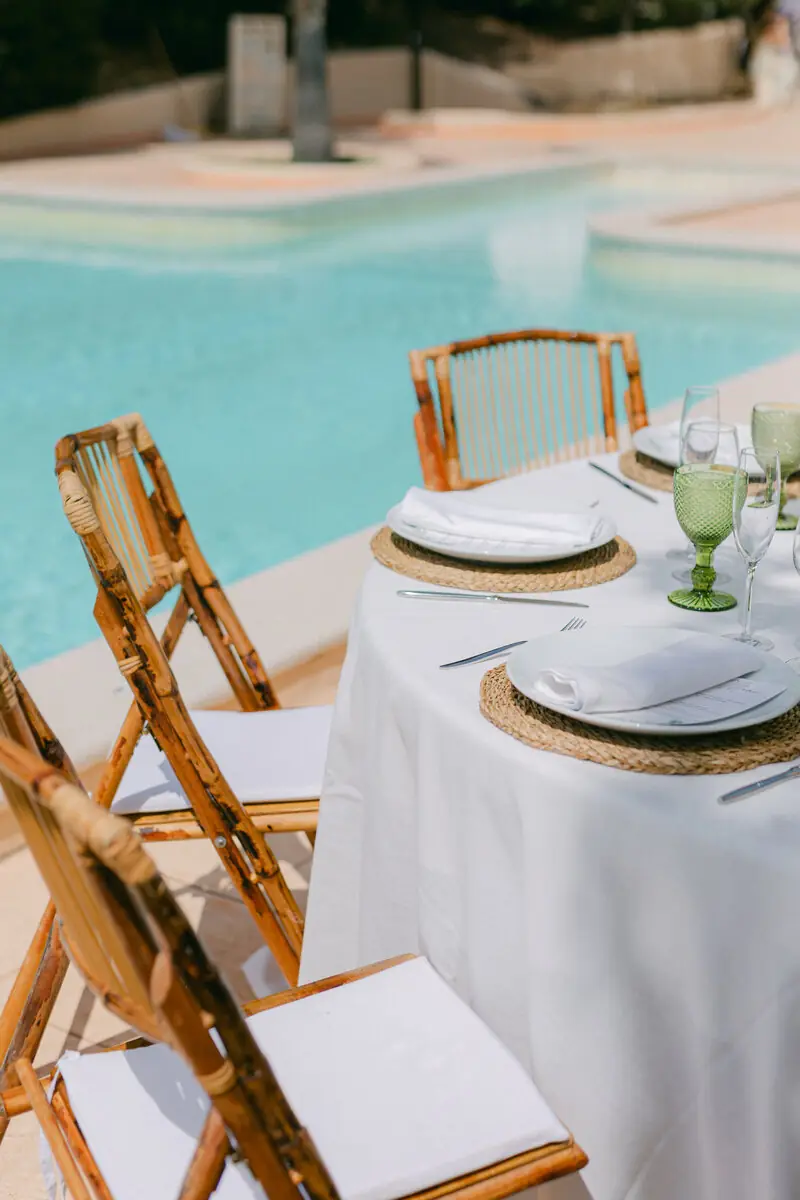 Mesa de boda junto a la piscina con bajoplatos dorados y cristalería verde, decorada por Les Recettes