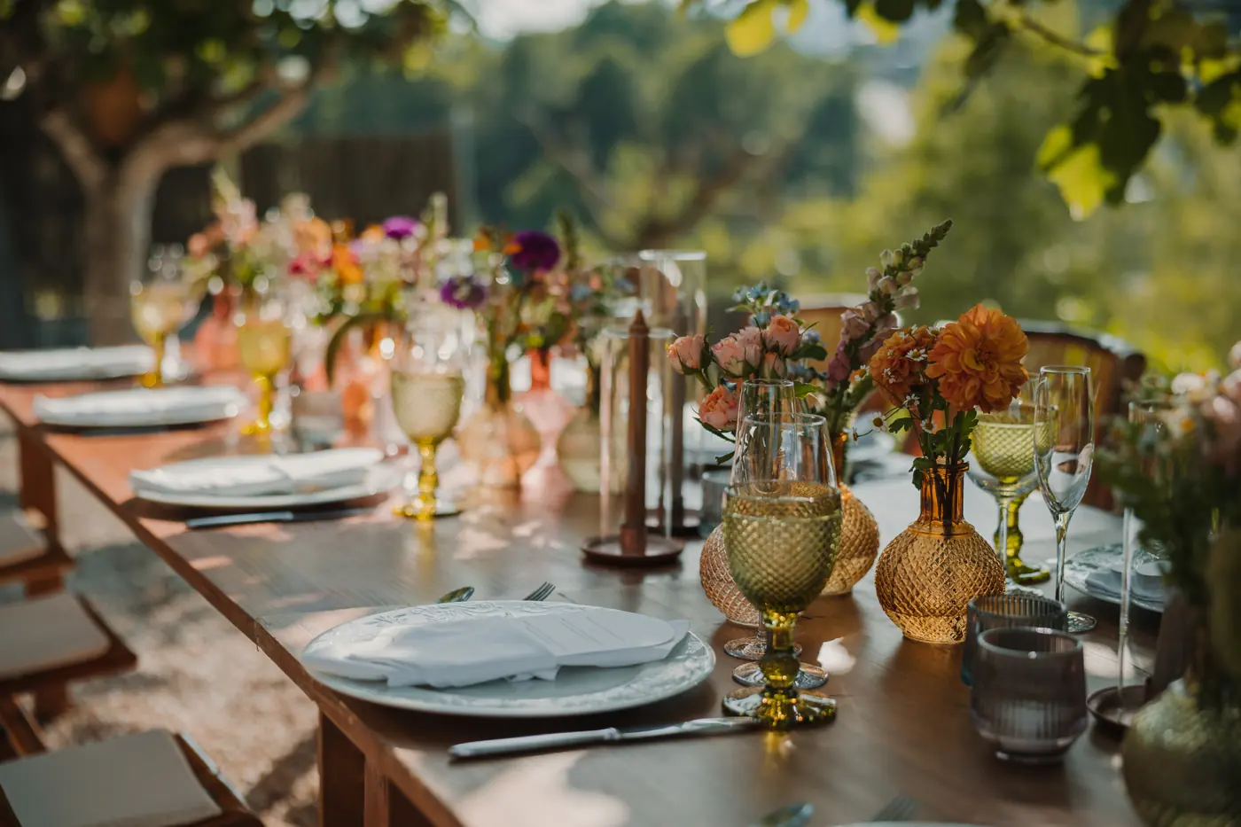 Mesa larga de boda decorada con candelabros dorados y flores de temporada bajo los árboles, en Cataluña