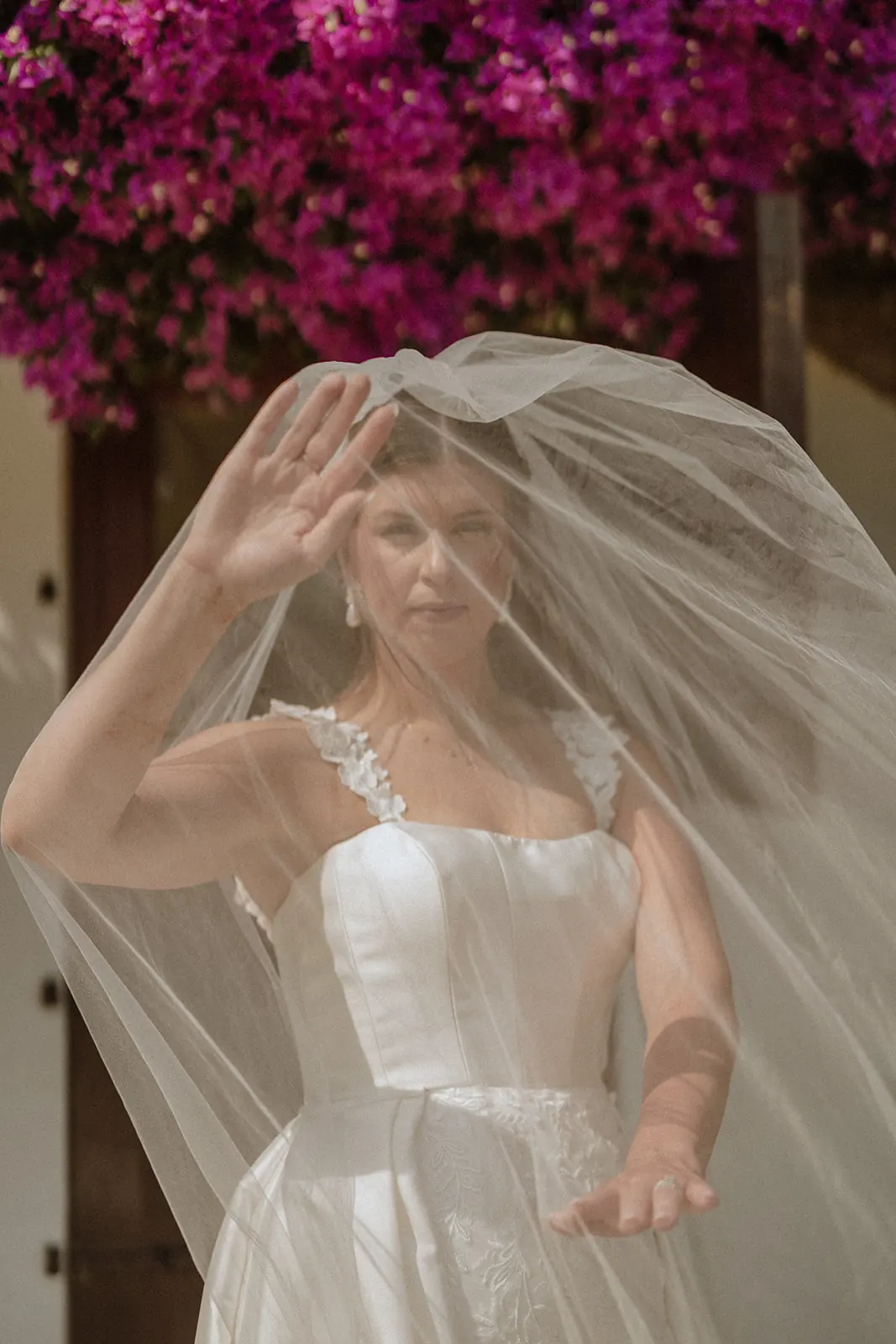 Una novia levantando su velo junto a una buganvilla en una finca de bodas de Barcelona
